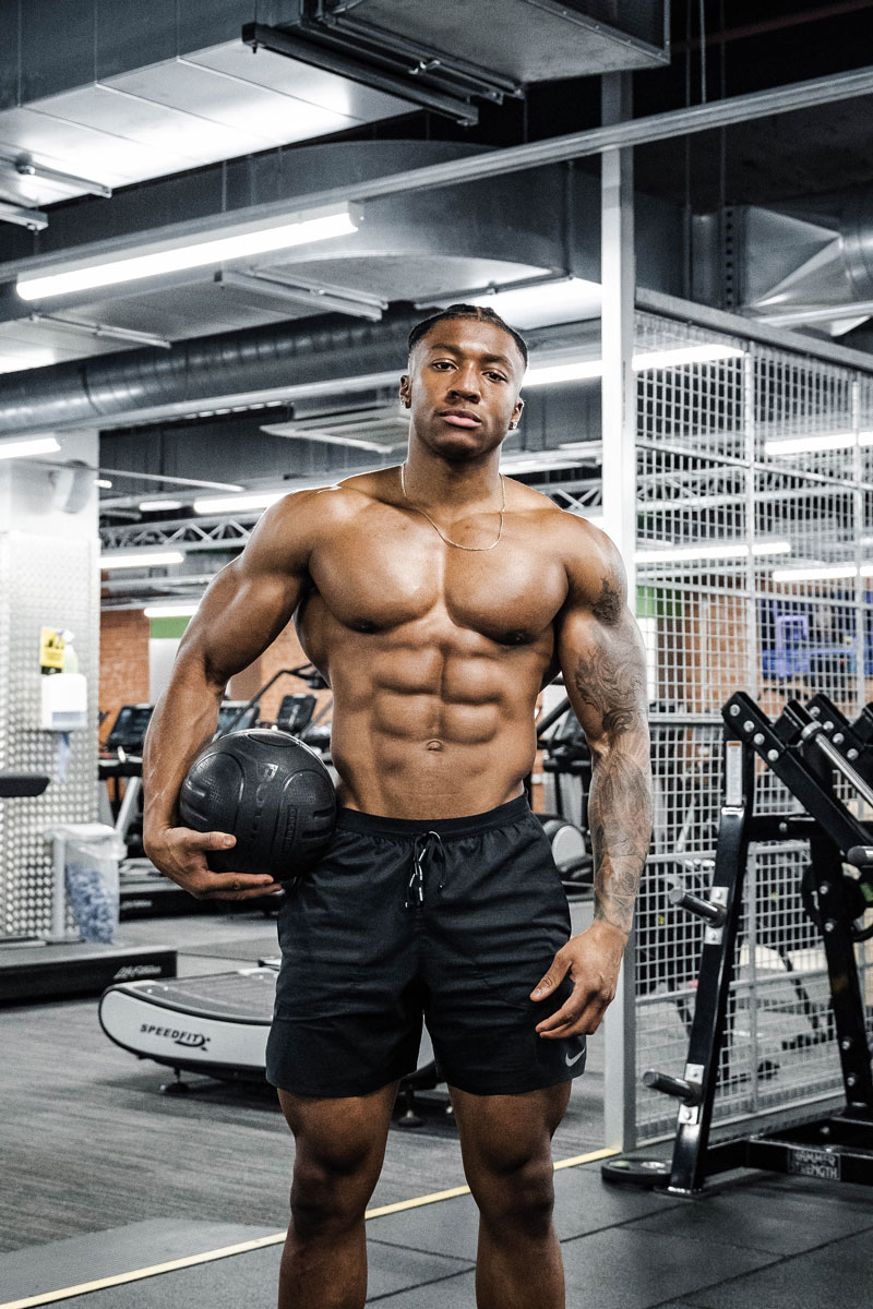 The coach is posing in the gym, holding a ball under his arm.